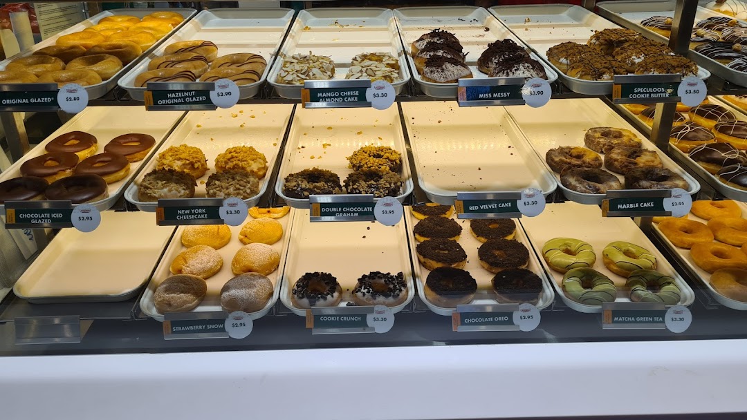 A vibrant display case showcasing a variety of Krispy Kreme donuts with their names and prices.