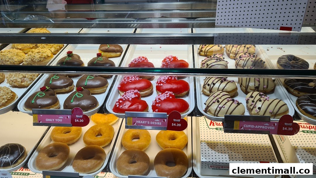 A vibrant display of Krispy Kreme donuts, including special heart-shaped varieties, in a glass case.