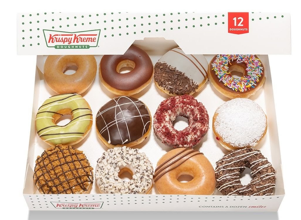 A dozen assorted Krispy Kreme doughnuts in a white box, showcasing various flavors.
