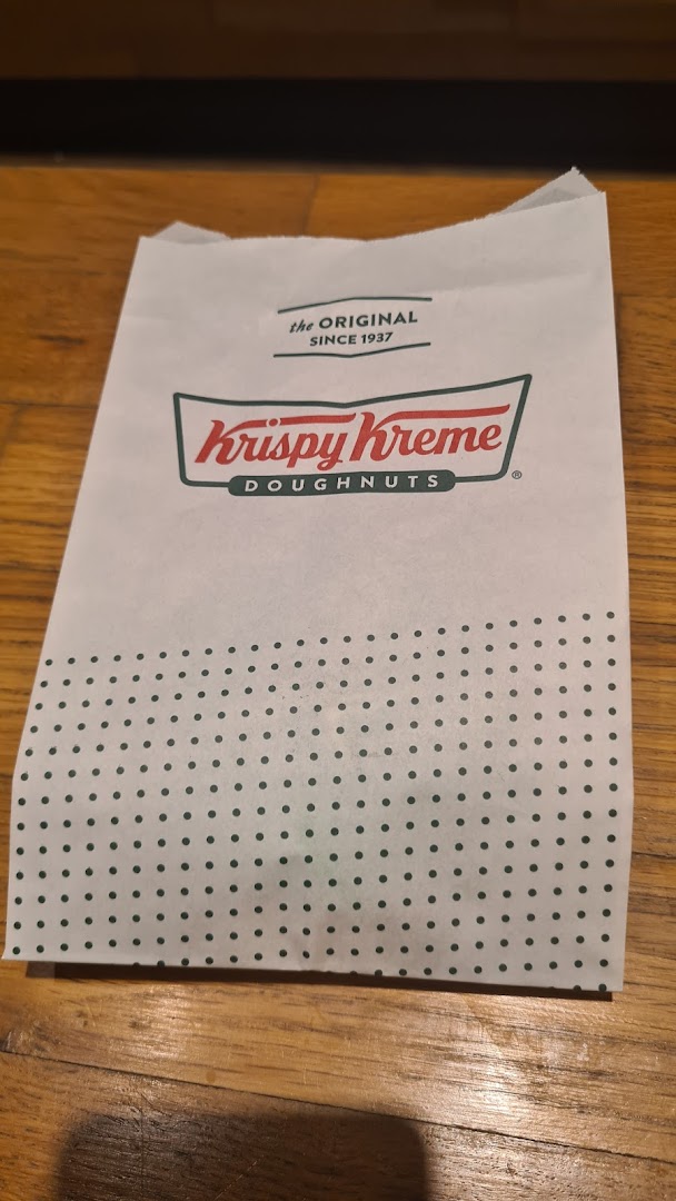A white Krispy Kreme Doughnuts paper bag with green polka dots on a wooden floor.