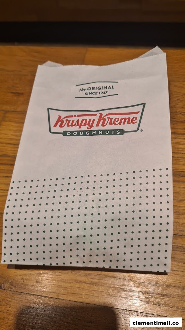 A white Krispy Kreme Doughnuts paper bag with green polka dots on a wooden floor.