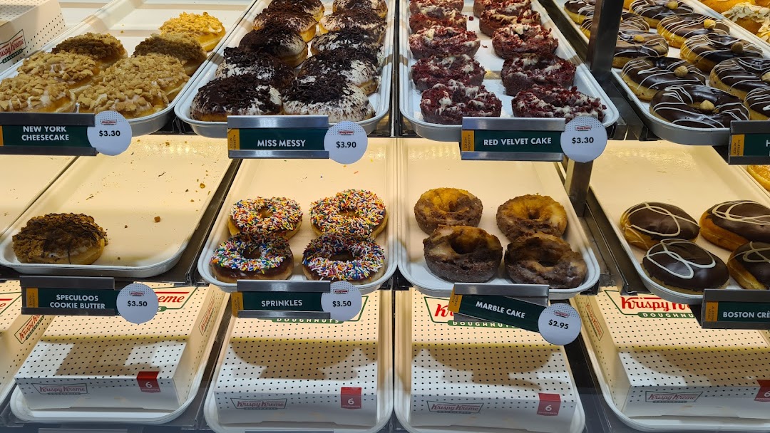 A vibrant display case showcasing a variety of Krispy Kreme donuts with their names and prices.