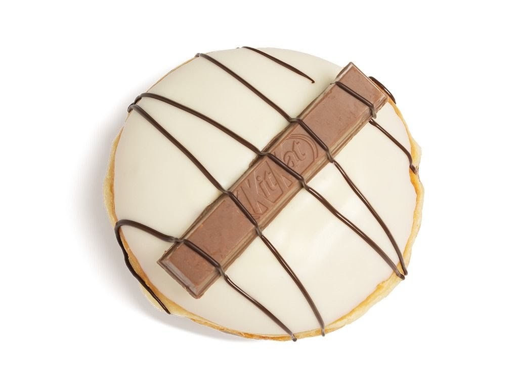 A Krispy Kreme donut with white icing, chocolate drizzle, and a Kit Kat bar on top.