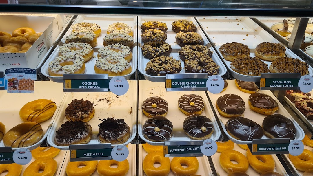 A vibrant display case showcasing a variety of Krispy Kreme donuts with visible prices.