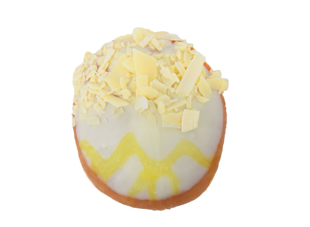 A Krispy Kreme donut with white icing, yellow drizzle, and white chocolate shavings on a white background.