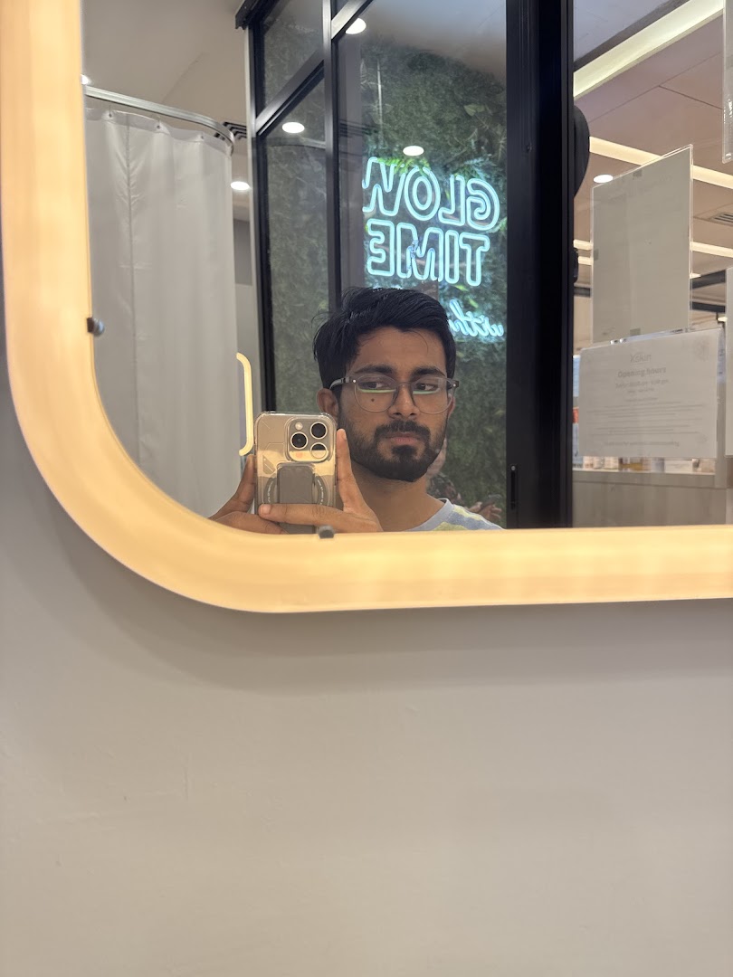 A person takes a selfie in a mirror inside Kskin, reflecting a 'GLOW TIME' neon sign and treatment area.