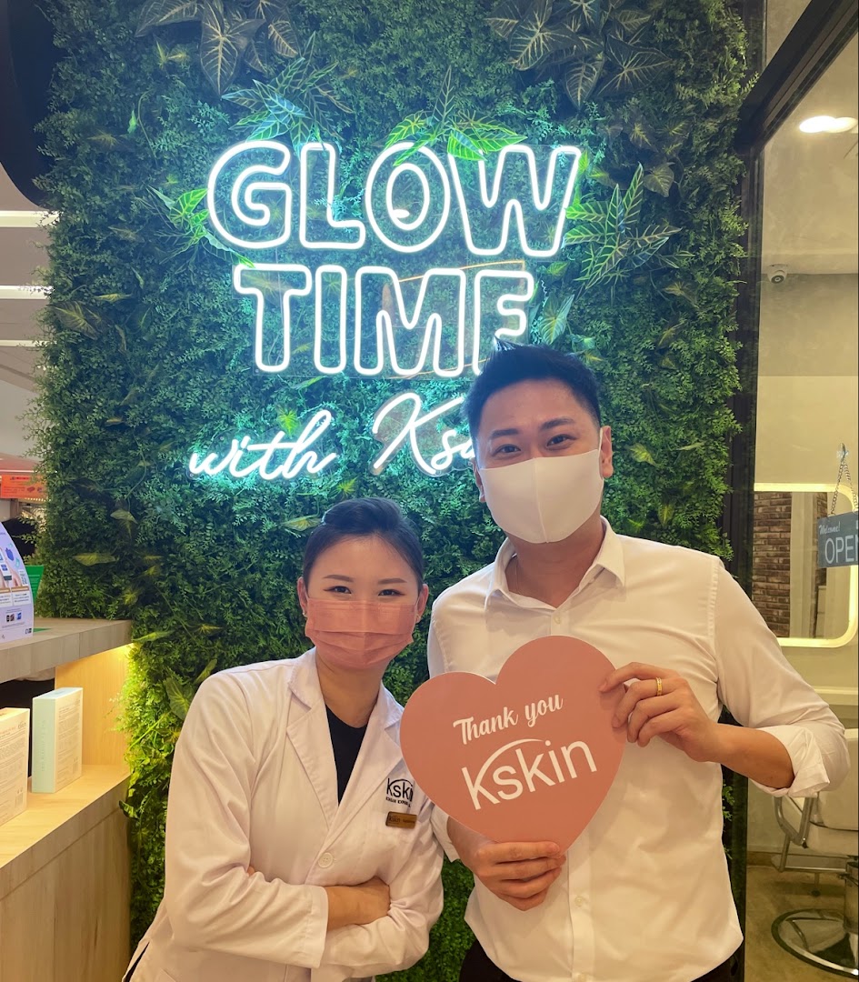 Two Kskin staff members smiling in front of a 'Glow Time' neon sign on a green wall.
