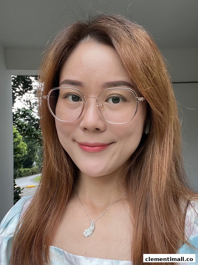 A close-up portrait of a smiling woman wearing glasses and a feather-shaped necklace.