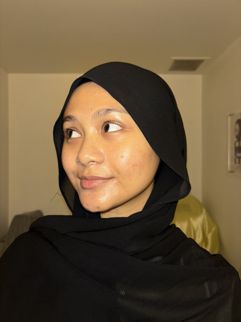 A young woman in a black hijab looking away, with a subtle smile.