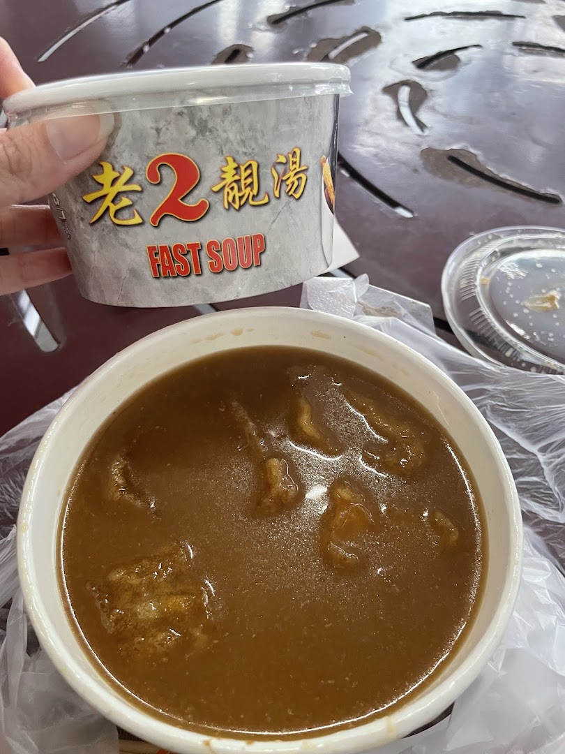 A hand holds a 'Fast Soup' container next to a bowl of rich, dark soup on a table.