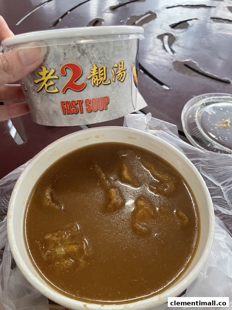 A hand holds a 'Fast Soup' container next to a bowl of rich, dark soup on a table.