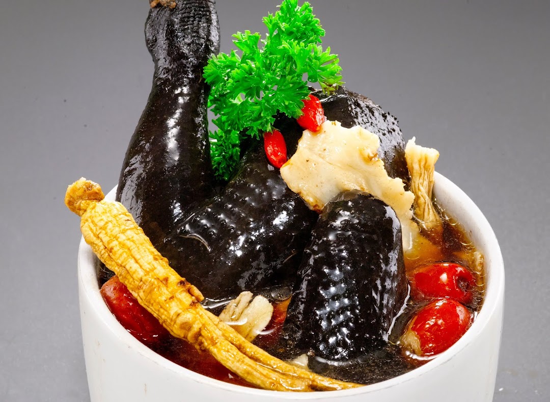 A close-up of a nourishing black chicken herbal soup with ginseng, goji berries, and other traditional ingredients.