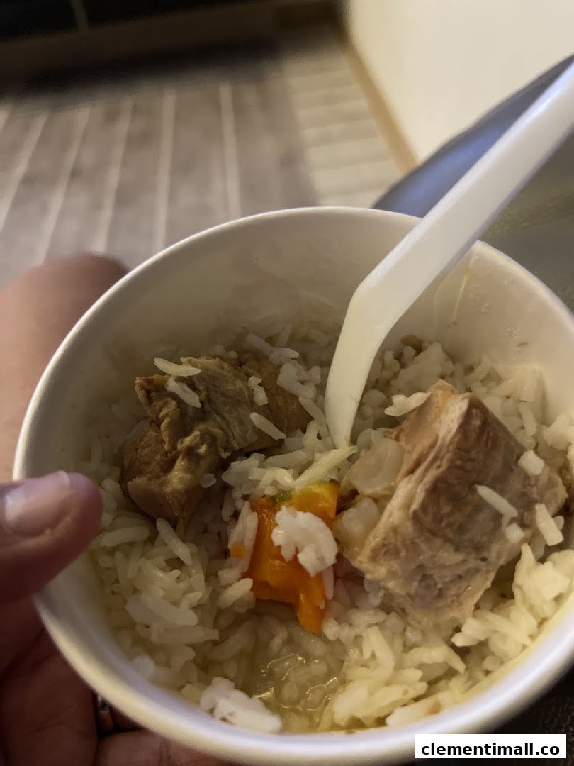 A close-up of a hearty meal in a cup, featuring rice, tender meat, and vegetables.