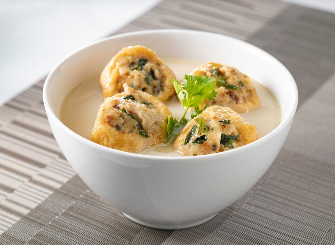 A white bowl filled with creamy soup and four pieces of stuffed fried tofu, garnished with cilantro.