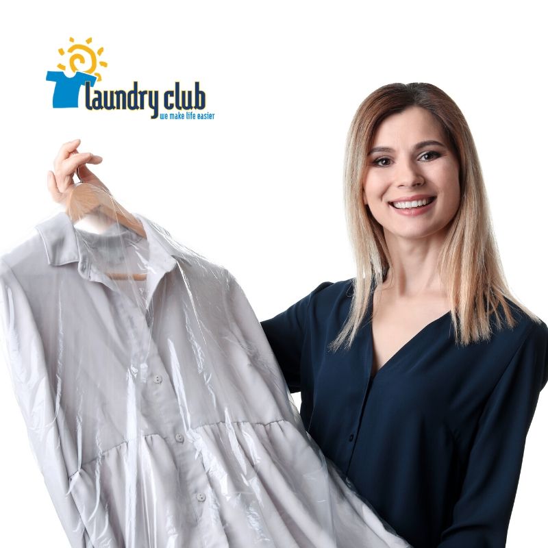 A smiling woman holds a freshly laundered garment from Laundry Club.