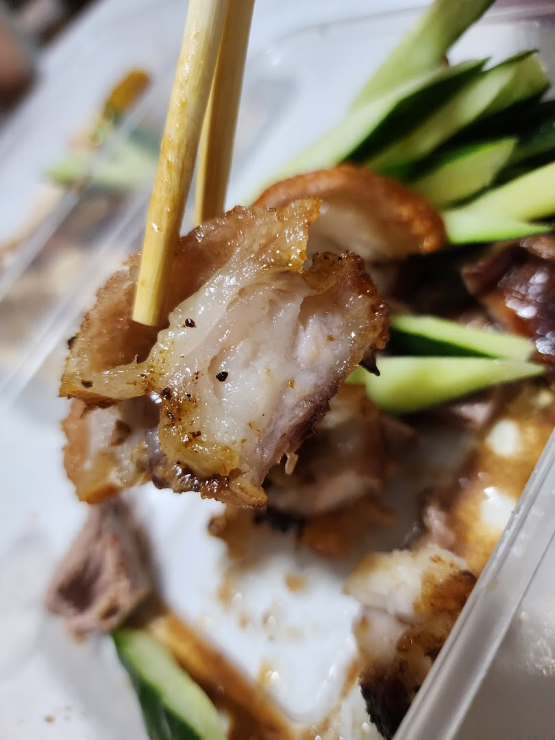 Close-up of a delicious piece of roasted meat, likely duck or pork belly, held by chopsticks.