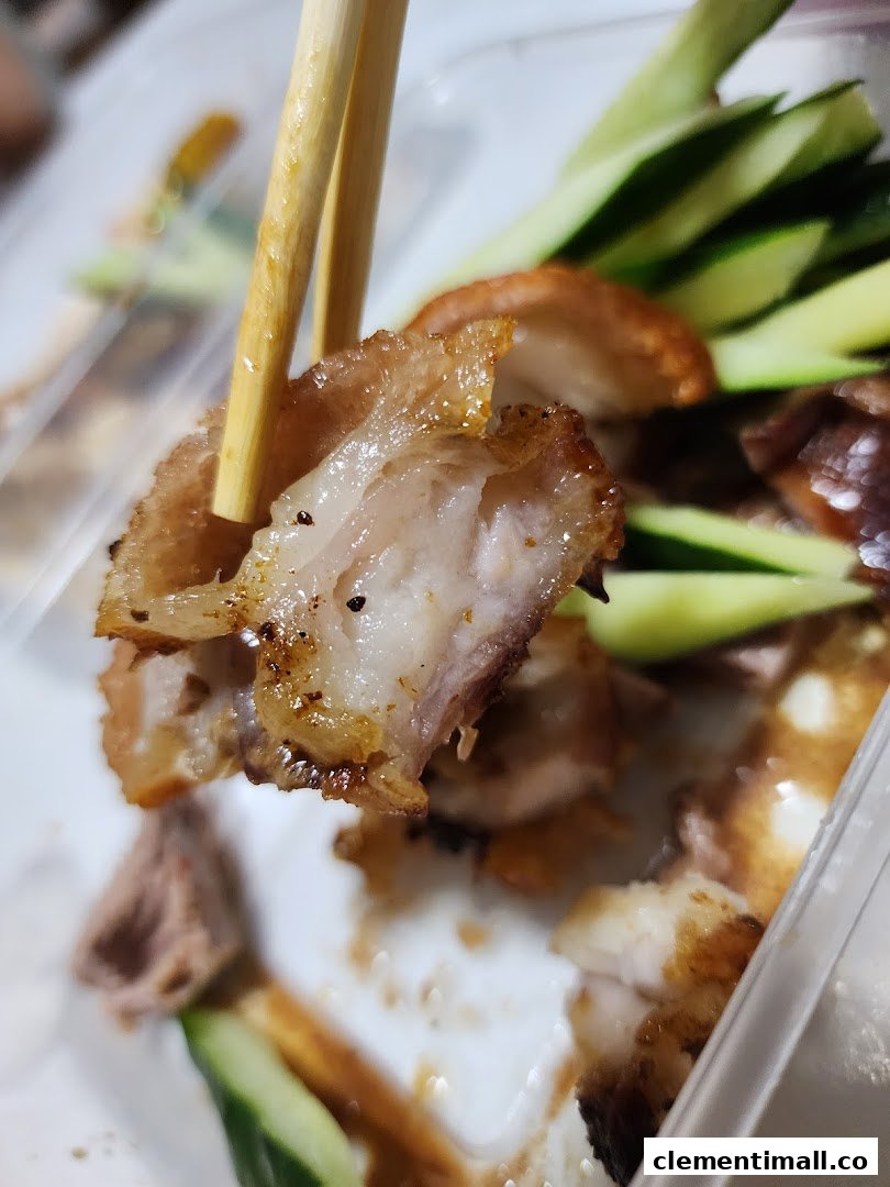 Close-up of a delicious piece of roasted meat, likely duck or pork belly, held by chopsticks.
