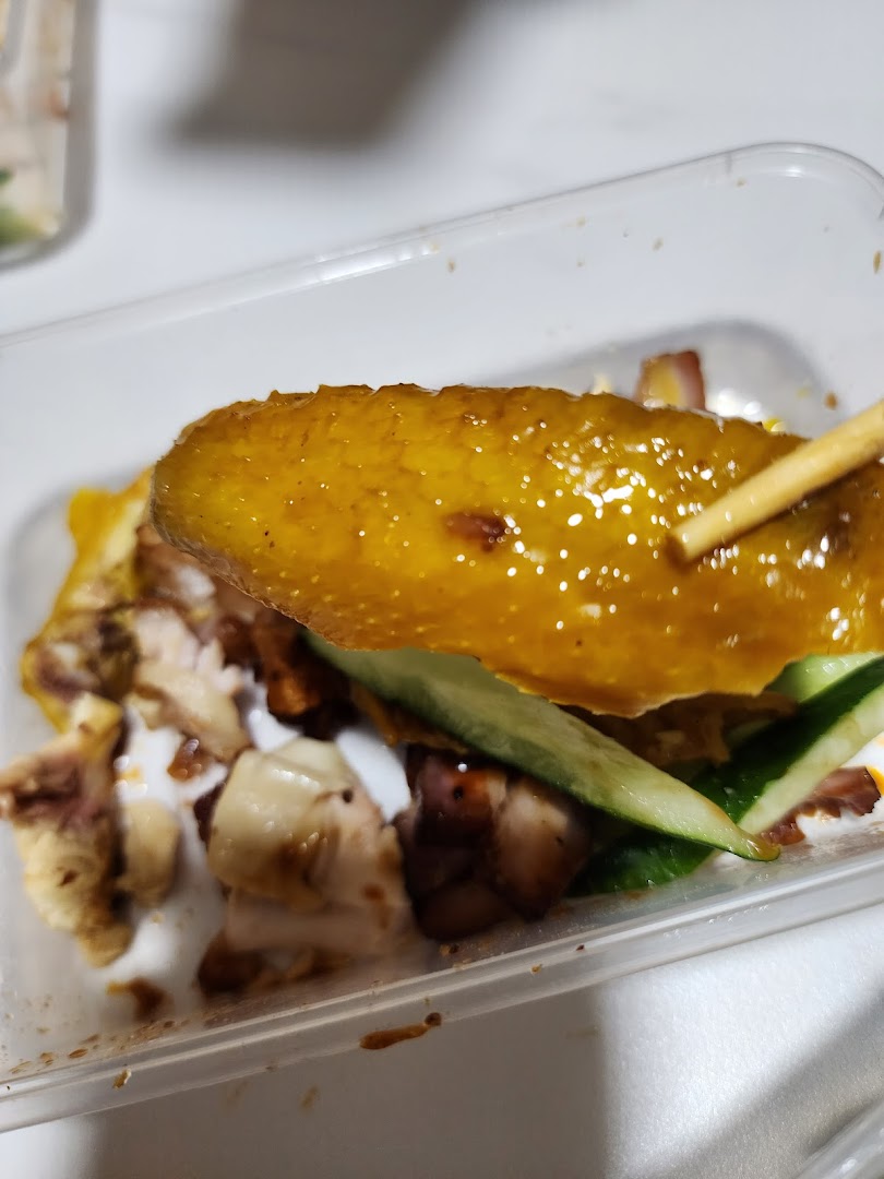 Close-up of a delicious piece of roasted duck skin with meat and cucumber, held by chopsticks.