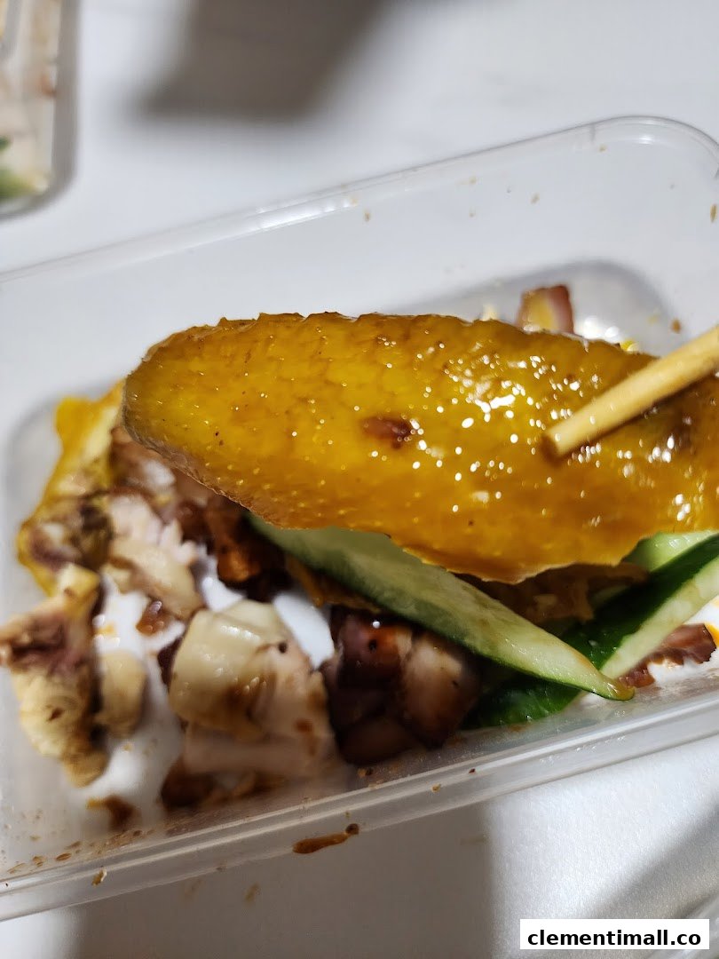 Close-up of a delicious piece of roasted duck skin with meat and cucumber, held by chopsticks.