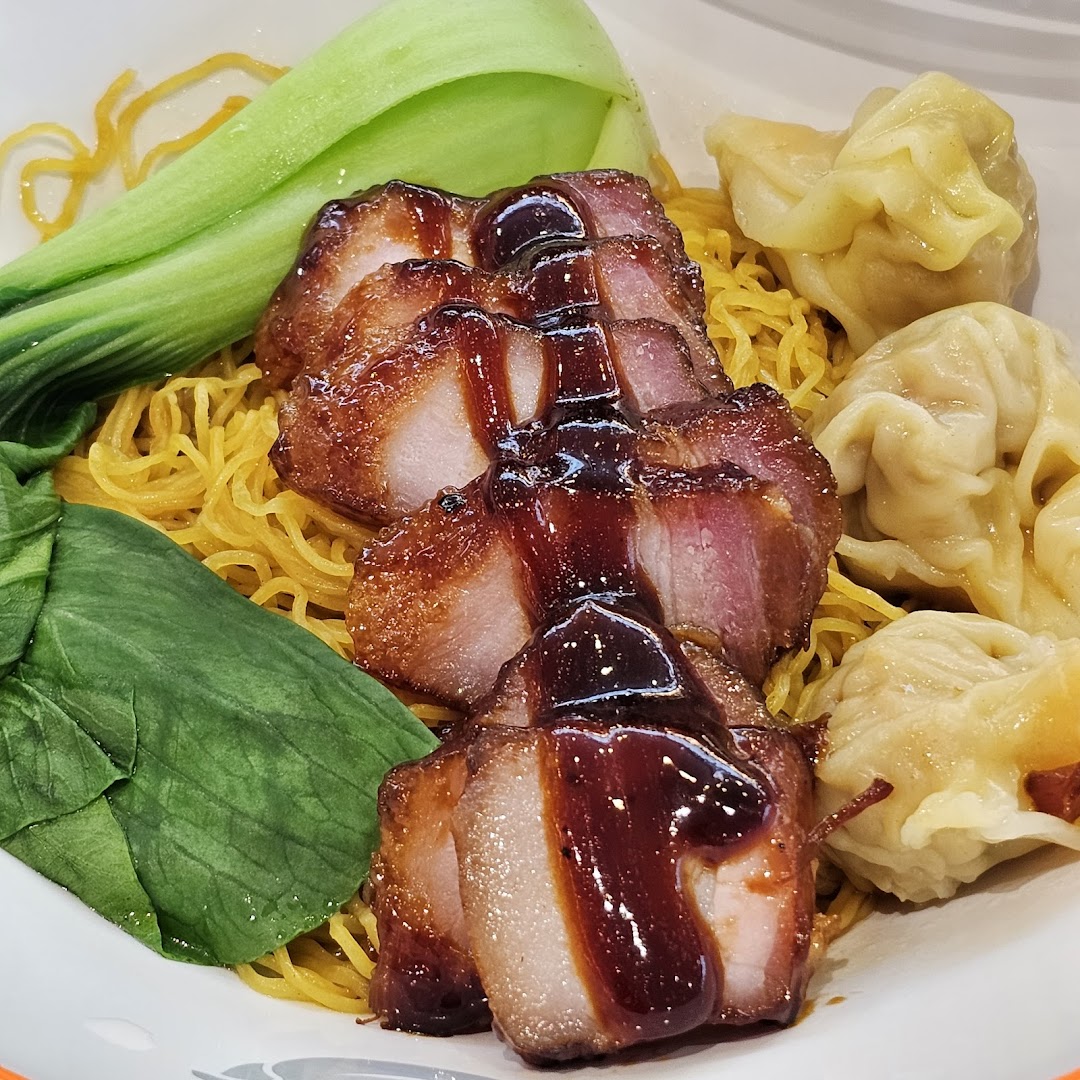 A close-up of char siu pork, noodles, bok choy, and wontons in a bowl.
