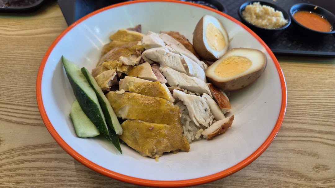 A plate of Hainanese chicken rice with poached and roasted chicken, braised eggs, and cucumber.