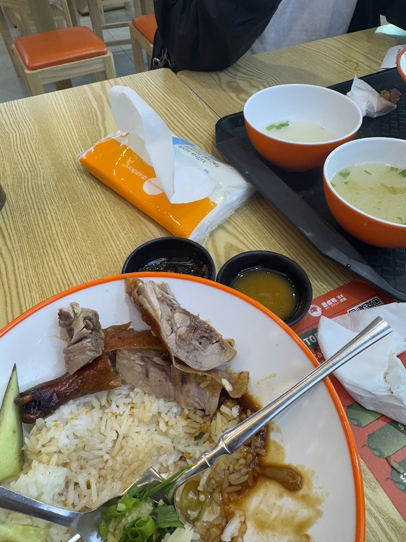 A close-up of a delicious duck rice meal with soup and condiments on a wooden table.