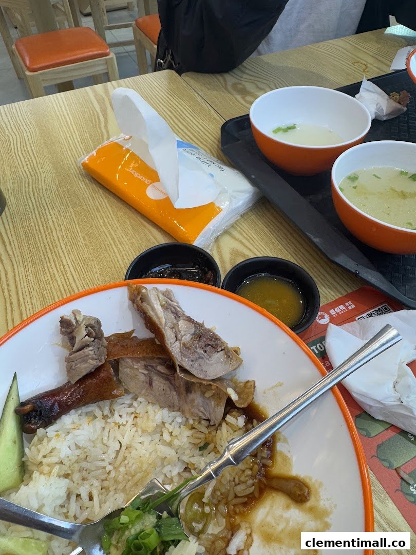 A close-up of a delicious duck rice meal with soup and condiments on a wooden table.