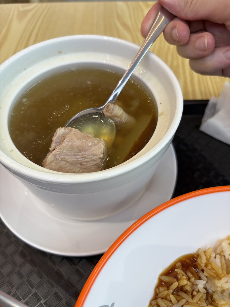 A close-up of a person enjoying a hearty bowl of soup with meat and a side of rice.
