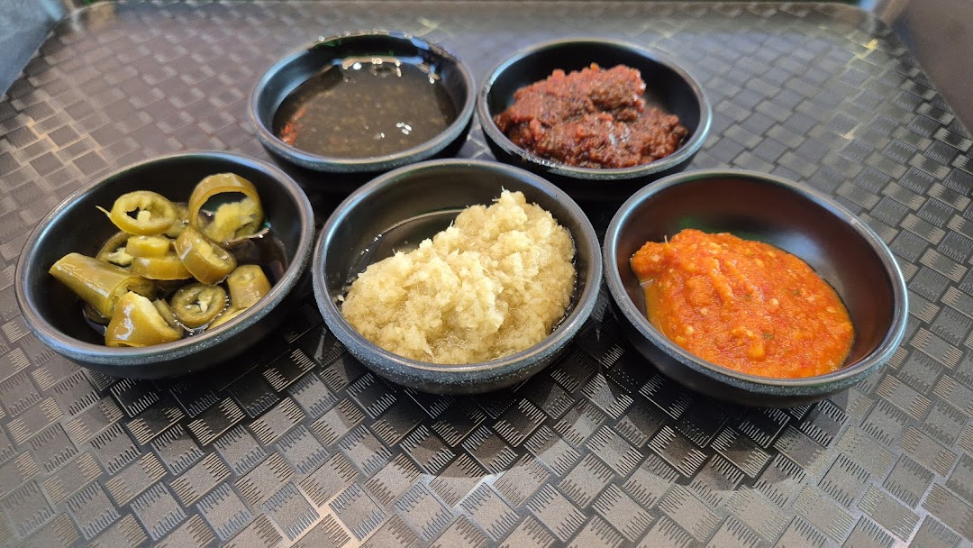 Five small bowls of various flavorful condiments including chili, garlic, and sauces on a textured tray.