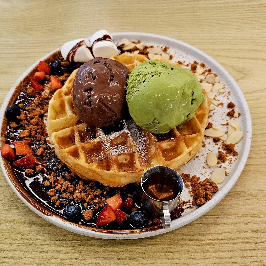 A delicious waffle topped with chocolate and matcha ice cream, berries, nuts, and syrup.