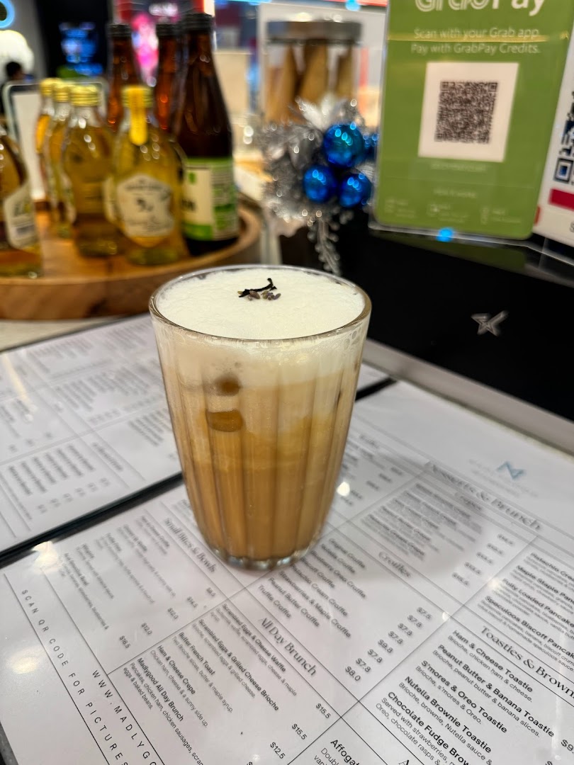 A refreshing iced drink with foam, placed on a detailed menu at MADLYGOOD.