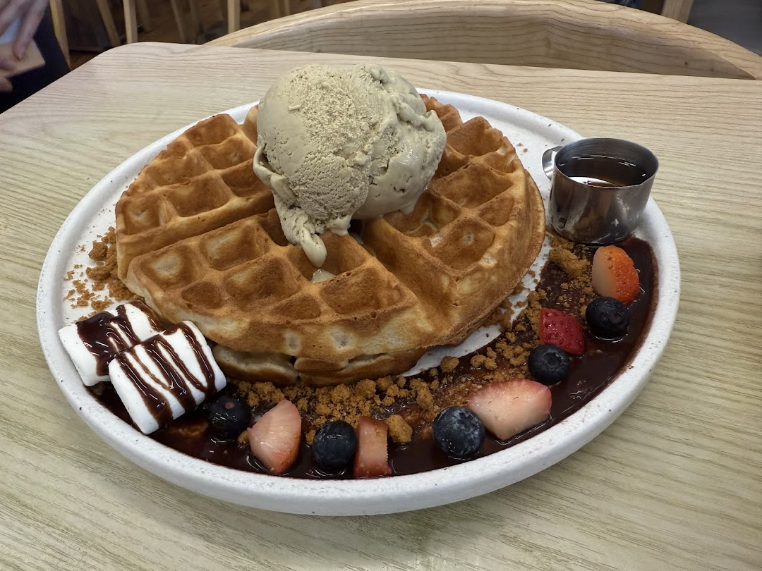 A delicious waffle dessert topped with ice cream, fresh berries, marshmallows, and chocolate sauce.