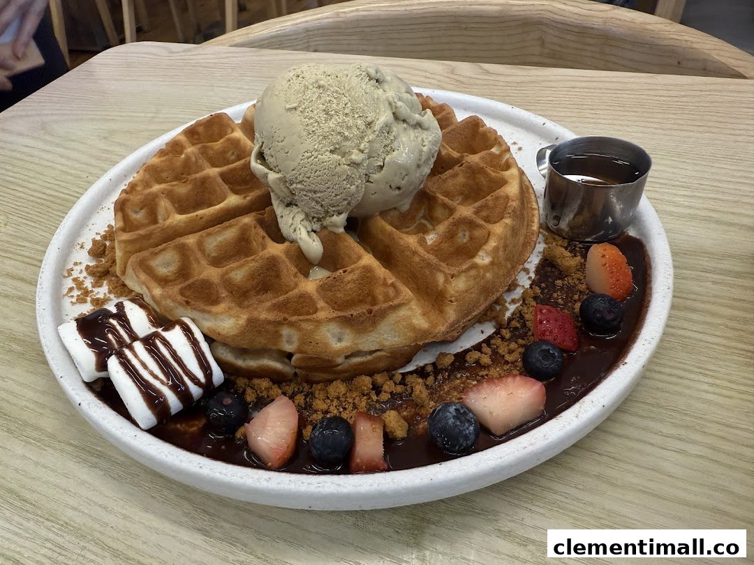 A delicious waffle dessert topped with ice cream, fresh berries, marshmallows, and chocolate sauce.