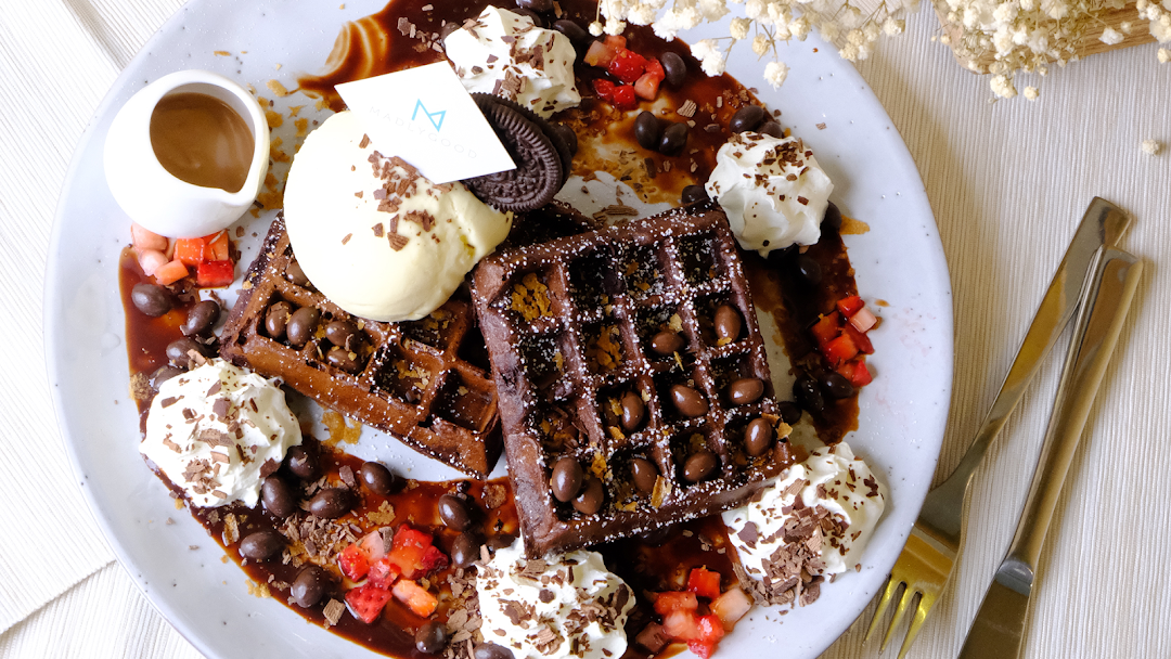 A decadent plate of chocolate waffles topped with ice cream, whipped cream, and various sweet garnishes.