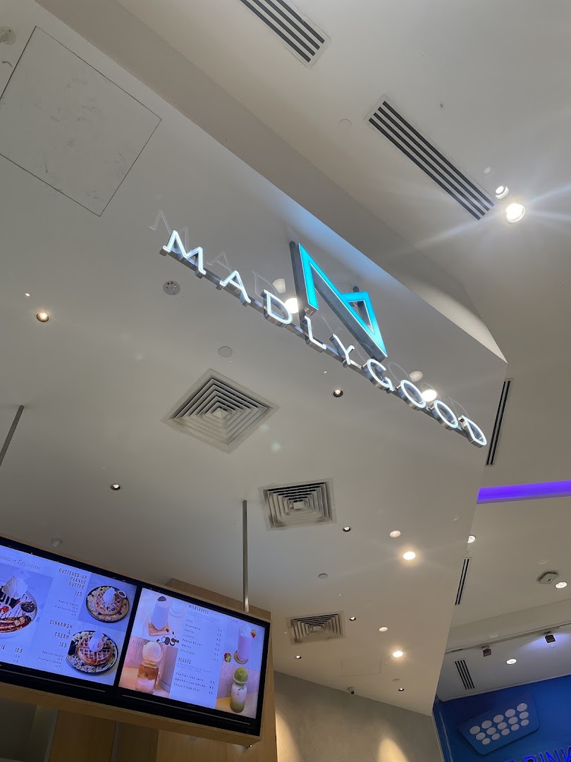 Interior view of MADLYGOOD featuring its illuminated logo and a digital menu board displaying waffles, milkshakes, and floats.