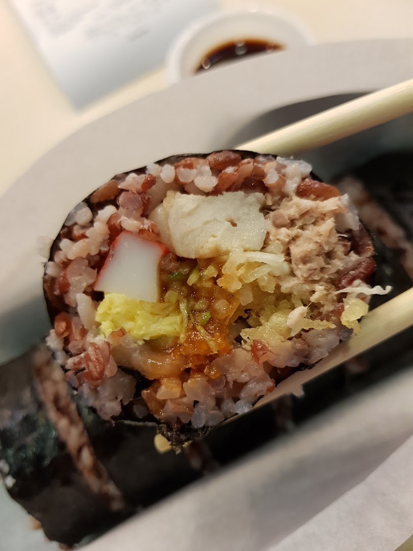 Close-up of a colorful sushi roll with various fillings, held by chopsticks.