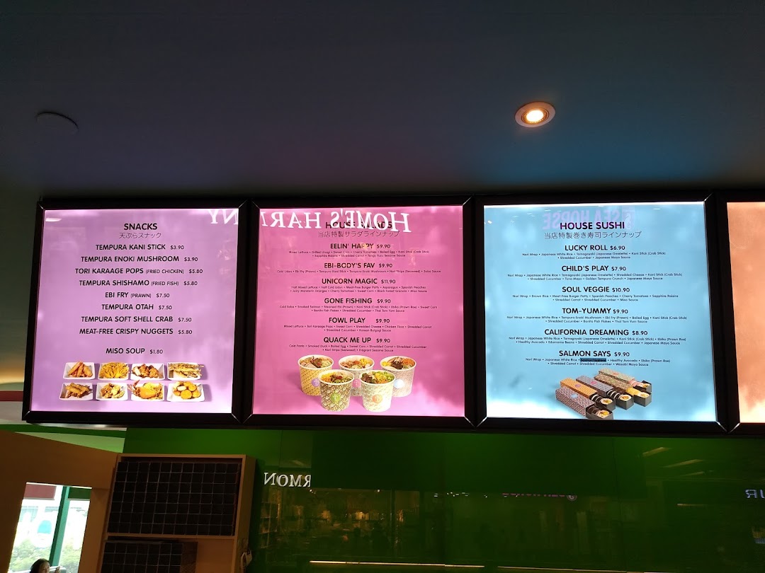 Three illuminated menu boards displaying a variety of snacks, salads, and sushi rolls with prices.