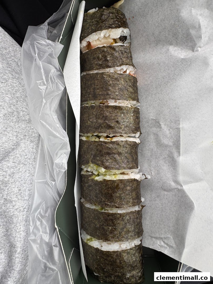 A long, cut sushi roll with various fillings, presented in a takeaway box from Maki-San.