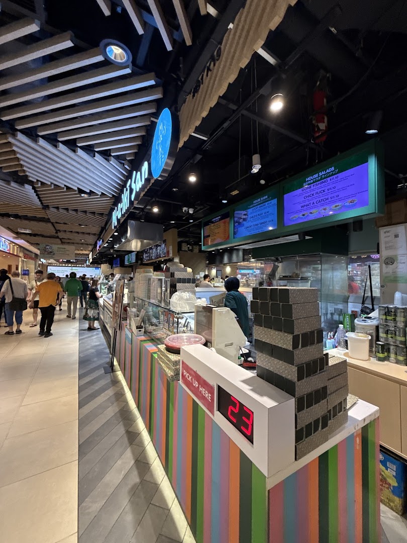 Maki-San's vibrant counter with digital menus, showcasing fresh sushi and salad options in a bustling mall setting.