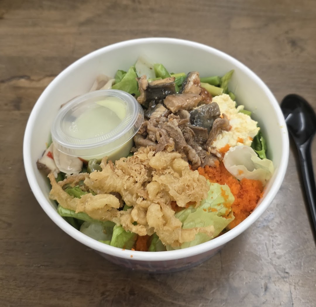 A vibrant custom sushi bowl or salad from Maki-San, featuring fresh greens, various toppings, and a side of dressing.