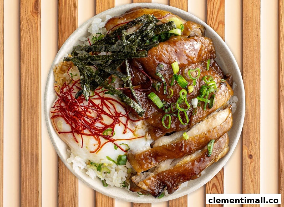 A delicious rice bowl featuring glazed chicken, a fried egg, seaweed, and spring onions.