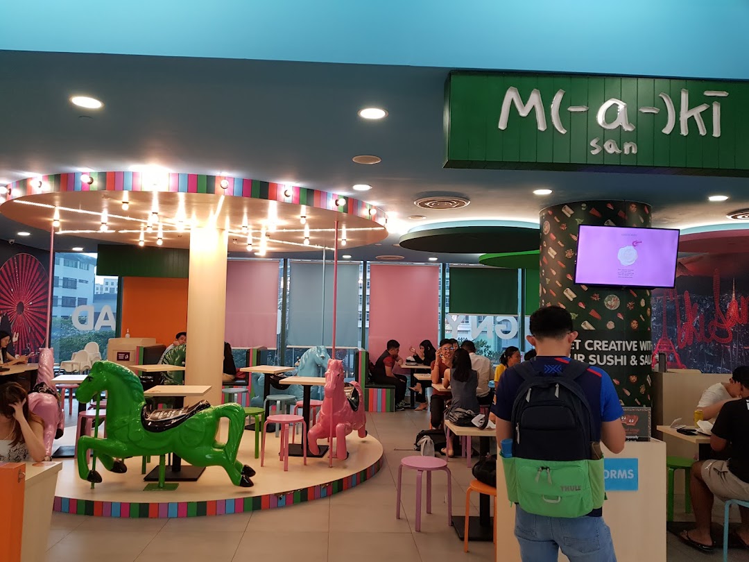 Vibrant interior of Maki-San featuring carousel-themed seating, colorful decor, and customers dining.