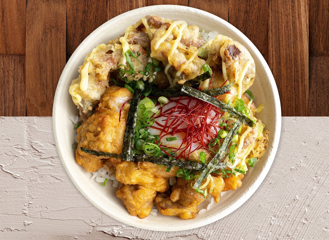 A close-up of a delicious Japanese rice bowl with fried chicken, tempura, egg, and fresh garnishes.