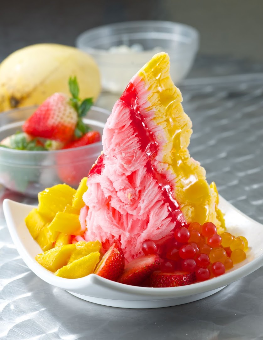 A vibrant shaved ice dessert with mango, strawberries, and popping boba, drizzled with syrup.