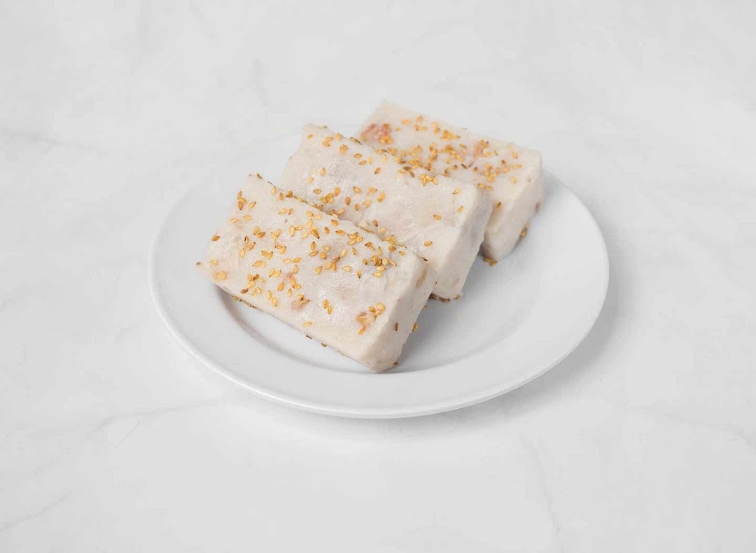 Three rectangular pieces of traditional dessert, possibly taro cake, topped with sesame seeds on a white plate.