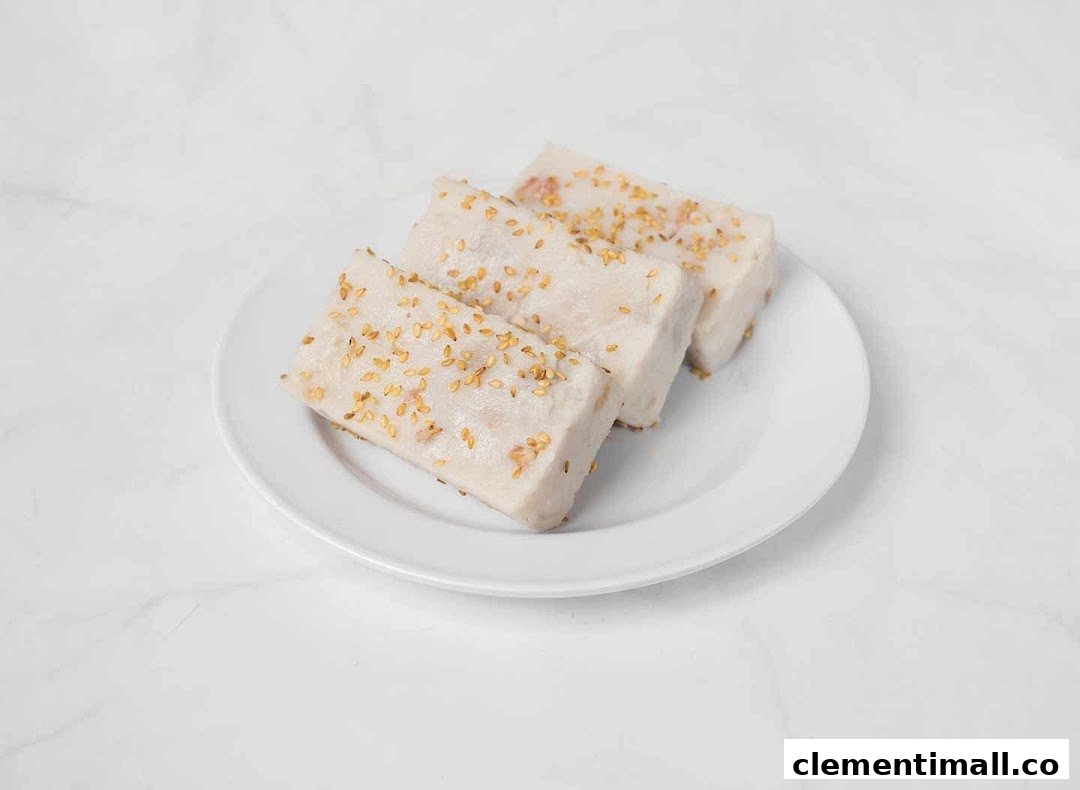 Three rectangular pieces of traditional dessert, possibly taro cake, topped with sesame seeds on a white plate.