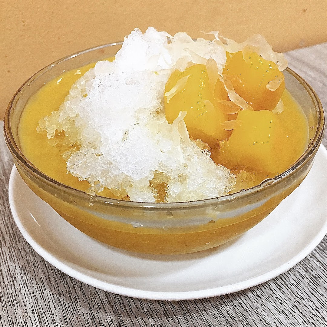 A vibrant bowl of mango dessert with shaved ice and fruit pieces.