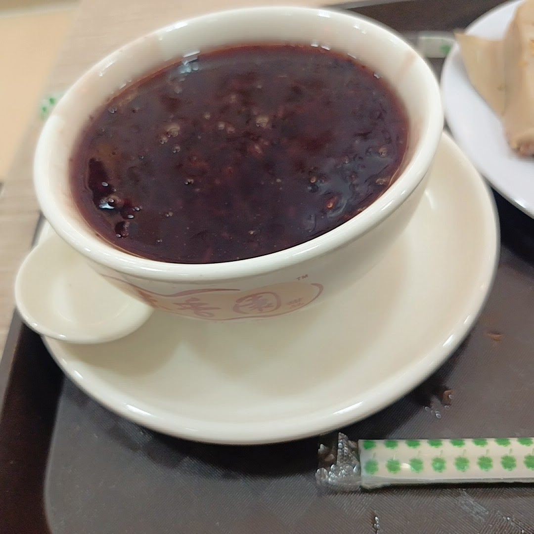 A close-up of a bowl of traditional black sesame dessert served on a tray.