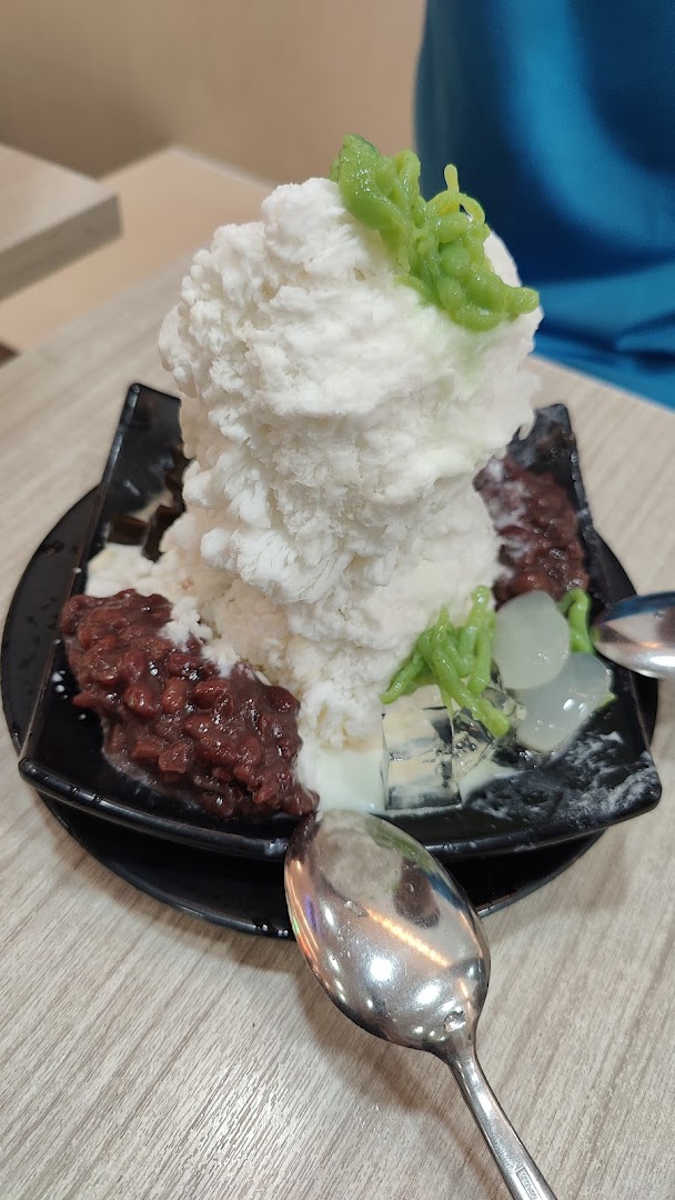 A close-up of a large bowl of refreshing shaved ice dessert with red beans, green cendol, and jellies.
