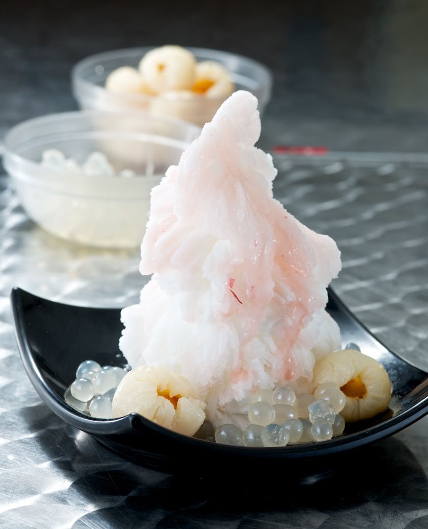 A refreshing shaved ice dessert with lychees and clear tapioca pearls in a black bowl.